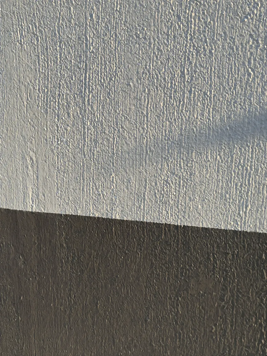 Detalhe de parede recém-pintada com acabamento texturizado claro e faixa grafite.
