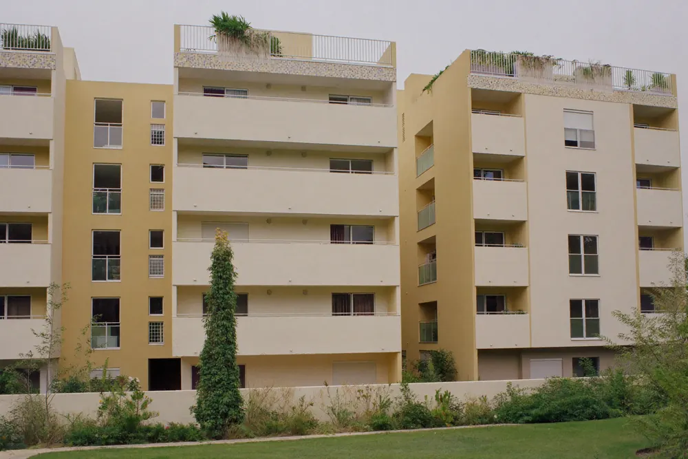 Condomínio residencial com fachadas claras recém-pintadas e jardim na frente.