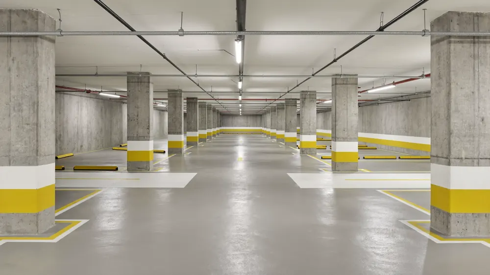 Garagem de subsolo com piso cinza, vagas demarcadas em amarelo e pilares com faixas.